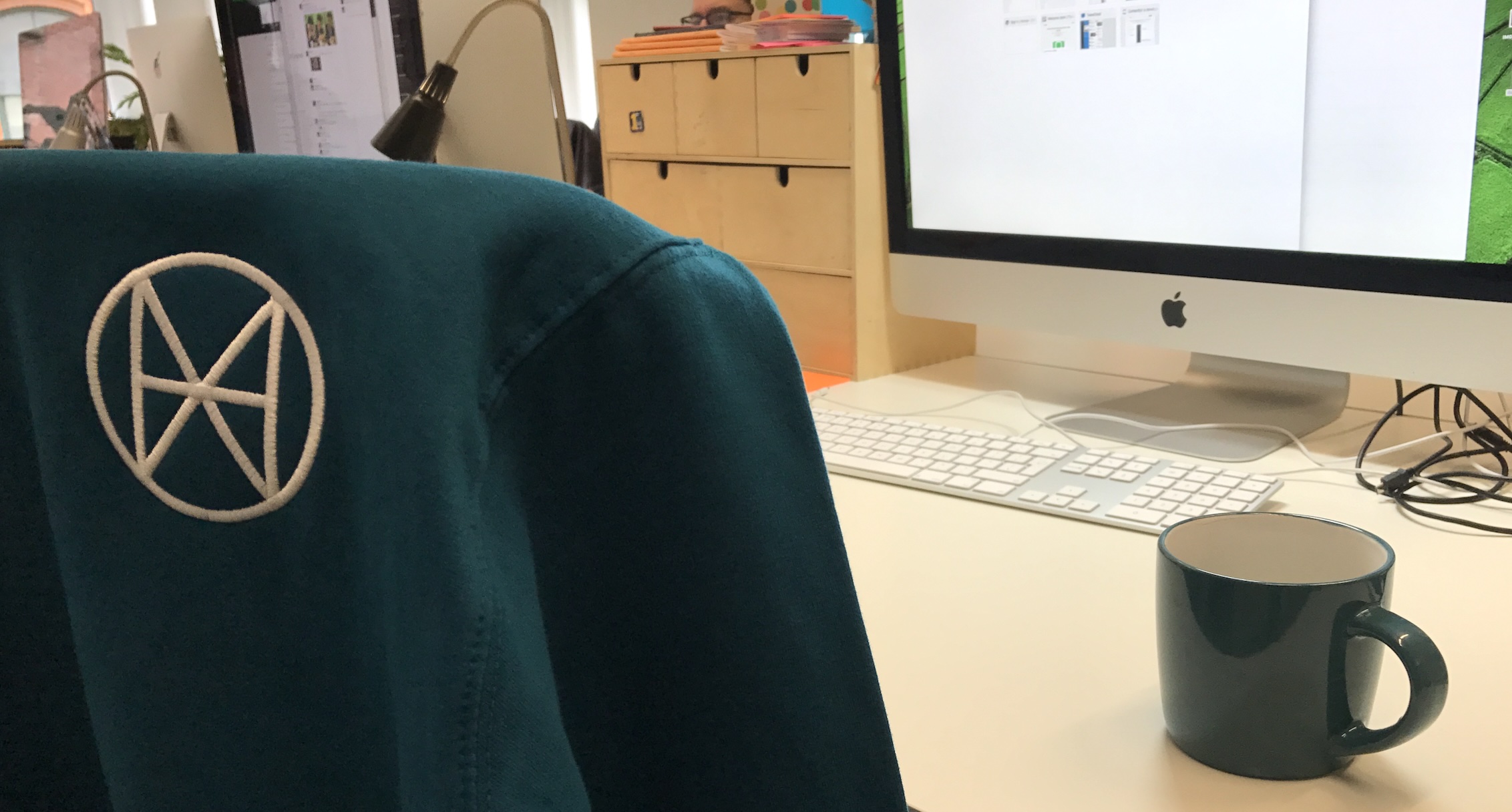 Human branded hoodie and brand colour mug on a desk